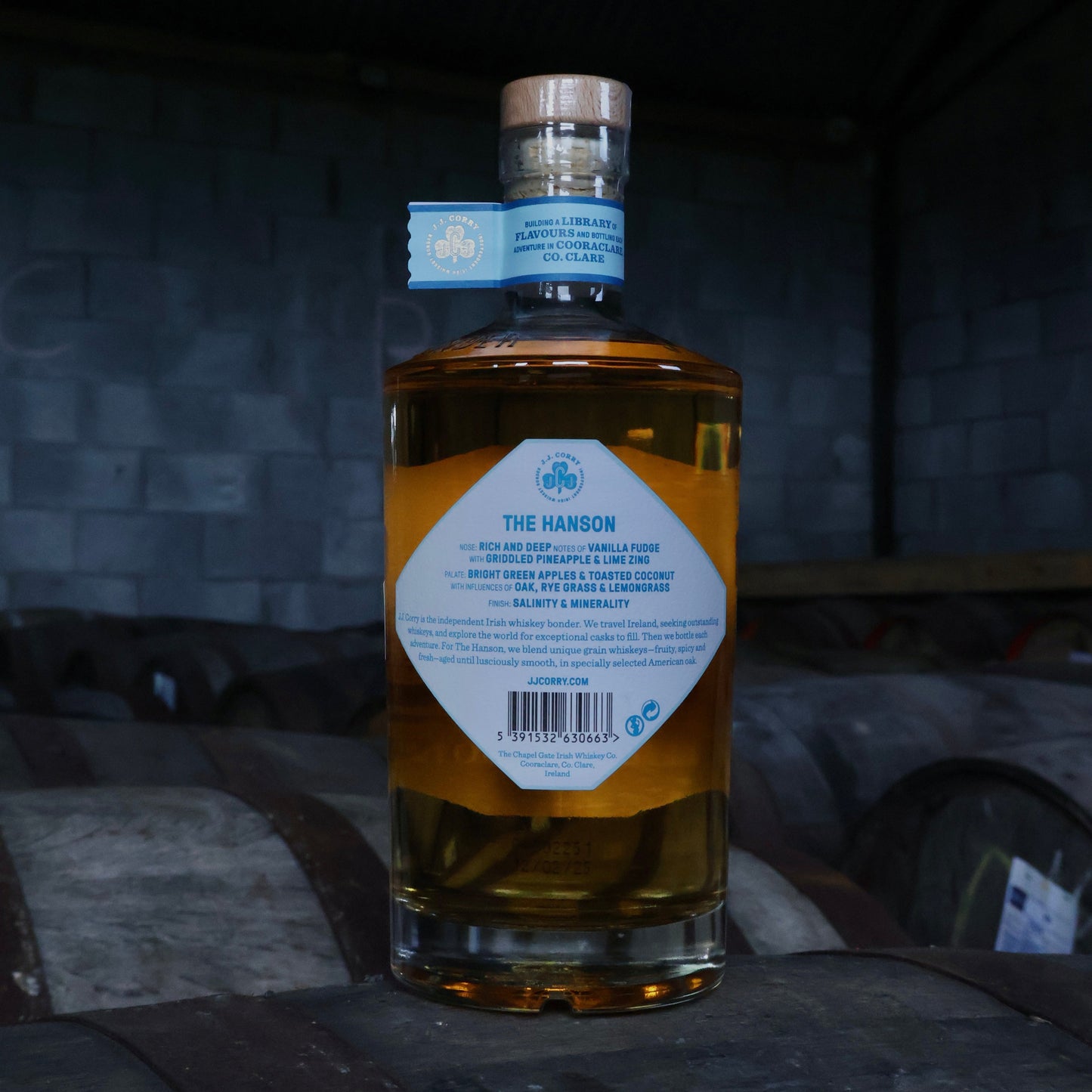 This is a photograph of a bottle of JJ Corry's The Hanson Irish whiskey on top of a wooden whiskey cask with a dark background