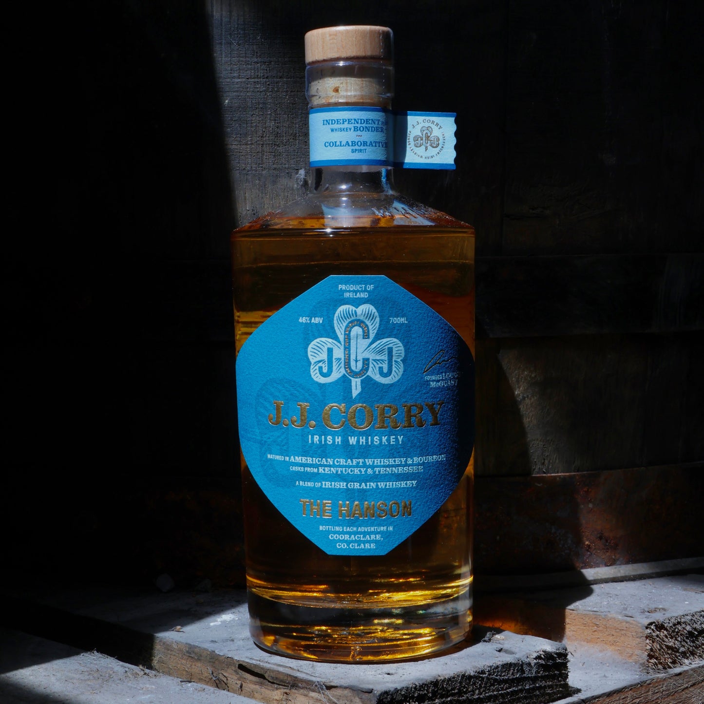 This is a photograph of a bottle of JJ Corry's The Hanson Irish whiskey on top of wood with a dark background